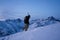 Brave traveler with backpack and a snowboard behind his back climbs winter mountain