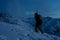 Brave traveler lights the way with a headlamp at night winter mountain. Snowboarder with backpack and a snowboard behind his back