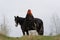 Brave woman with red hair in black cloak on friesian horse