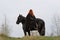 Brave woman with red hair in black cloak on friesian horse