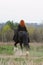 Brave woman with red hair in black cloak on friesian horse