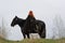 Brave woman with red hair in black cloak on friesian horse