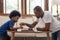 Brazilian Father and little boy playing chess on table at home together. Happy Black African American Family engaged in board game