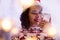 Brazilian girl wearing christmas hat and seasonal sweater checking social media in smartphone at home. decor blur lights