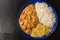 Brazilian tenderloin stroganoff with rice and potato sticks in a blue plate isolated in dark wood background  seen from above