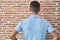 Brazilian young man standing over brick wall standing backwards looking away with arms on body