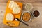 Bread on cutting board, spoon, bowls with sunflower seeds and raisin, bowl with peanut butter on table. Top view