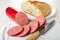 Bread in plate, sausage in polyethylene pack, slices of sausage, knife on cutting board on wooden table