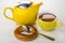 Bread ring, yellow teapot, cup of tea and spoon