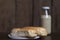 Bread on a white plate sits on a wooden board table with milk in a bottle behind it