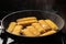 Breaded fish sticks in a frying pan. Preparation of frozen fish sticks. Fast food. Dark background