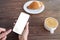 Break time. Lady holding smartphone with blank screen while drinking coffee and eating croissant at cafe, mockup for