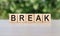 BREAK word written on wooden blocks. The text is written in black letters and is reflected in the mirror surface of the table.
