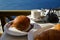 Breakfast with Aegean sea view and morning sunlight including hot tea, croissant and chocolate brioche bun on white marble table