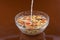 Breakfast cereals, oatmeal with candied fruits and nuts in a glass bowl and pouring milk, brown background