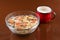 Breakfast cereals, oatmeal with candied fruits and nuts in a glass bowl and red cup milk, brown background