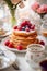 Breakfast experience with stacks of fluffy pancakes adorned with raspberries and powdered sugar, accompanied by vases of beautiful