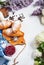 Breakfast with fresh croissants, glass of coffee, milk, strawberry jam and flowers on a white wooden background