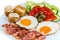 Breakfast fried egg fresh vegetables fried bacon and olives on a white plate