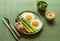 Breakfast fried eggs with fresh asparagus and ham (jamon), herbs in plate on green background. Delicious hearty brunch