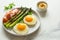 Breakfast fried eggs with fresh asparagus and ham (jamon), herbs in plate on a white background. Delicious hearty brunch