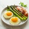 Breakfast fried eggs with fresh asparagus and ham (jamon), herbs in plate on white background. Delicious hearty brunch