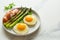 Breakfast fried eggs with fresh asparagus and ham (jamon), herbs in plate on white background. Delicious hearty brunch