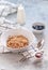 Breakfast, hand pours milk from a jug into muesli in a deep dish. Next to blueberries and jam on a blue-gray concrete background