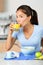 Breakfast at home Asian woman drinking fresh cold pressed orange juice beverage during cereal meal in kitchen. Vertical