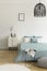 Breakfast on a metal table in front of a bed with sage green bedding in a natural bedroom interior. A beige drawer cabinet by the