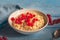 Breakfast of milk oatmeal with red currants in a deep plate on a wooden tray