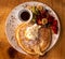 Breakfast pancake, maple syrup, cream, fresh fruit served on white plate atop wooden table