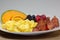 Breakfast plate of bacon, cantaloup slice, orange slices, blackberries, raspberries and blueberries on the kitchen table waiting t