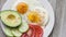 Breakfast plate with sunny side up fried eggs, tomato slices and avocado on rustic wooden surface