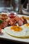 Breakfast presentation closeup image - fried eggs, sausages and aditions. Blurry food and drinks background