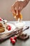 Breakfast set concept. Faceless photo of someone`s hand dipping pancake in sour cream. Pancake tower with fresh raspberries and