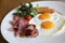 Breakfast set with fried eggs, bacon, sausages, beans, toasts, fresh salad and fruit on a plate