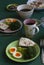 Breakfast for two: boiled sliced â€‹â€‹egg, broccoli, bread with butter and spices, black coffee and oatmeal with nuts and apples