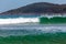 Breaking ocean wave with forested hill in the background.