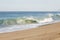 Breaking tube wave on sandy beach with foamy backwash, open expanse of ocean