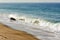 Breaking wave with backwash on sandy beach with boulder and footprints