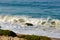 Breaking wave on to foaming backwash with ocean swells, sand, rock, and iceplant