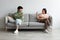 Breakup and divorce concept. Young married Asian couple having fight, sitting on opposite sides of couch at home