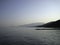 Breakwater on the shore of a calm sea against the background of coastal mountains in the haze of the sky in the distance in the