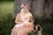 Breast feeding: Young hippie mother breastfeeds her baby girl child in city park sitting under a tree on a green grass