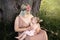 Breast feeding: Young hippie mother breastfeeds her baby girl child in city park sitting under a tree on a green grass