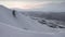 Breathtaking aerial view of white snow on black mountain rocks at sunset. Delicate pink dawn behind grey clouds in the