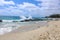 A breathtaking shot of the deep green ocean water and the beach and the waves crashing against the rocks with blue skies and cloud