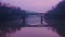 A breathtaking view of a bridge enveloped in a purpletinted sky reflecting its graceful curves onto a calm river below