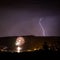 Breathtaking view of flash of lightning in dark purple sky with fireworks at a distance